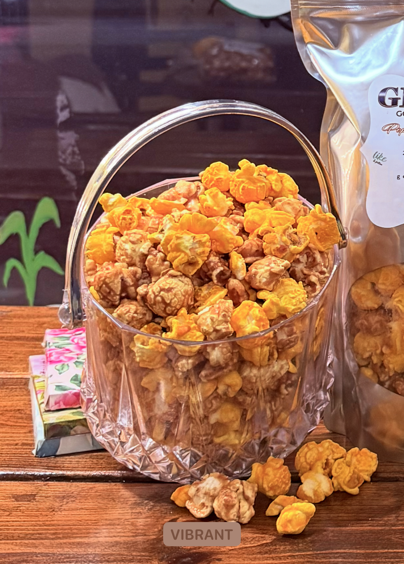 Clear glass bowl filled with popcorn on a wooden surface, with a bag of popcorn in the background.